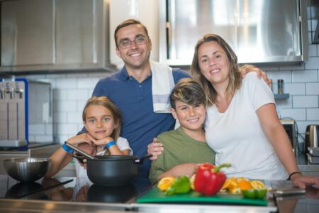 Parent cooking in modern kitchen while child plays nearby, representing multitasking scenarios where voice shopping thrives