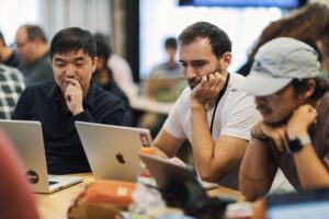 Engineers collaborating around a laptop screen during a team standup meeting